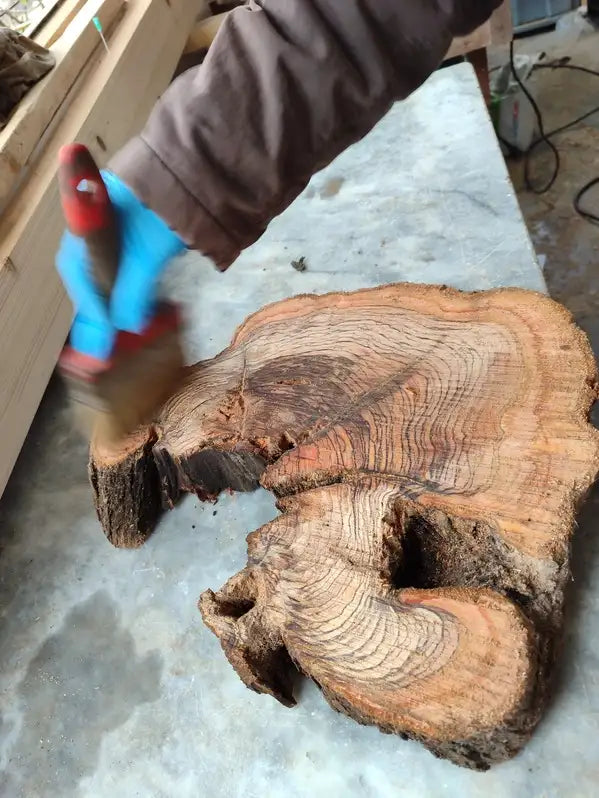 A rustic, irregularly shaped wooden slab with a natural, bark-encrusted edge and visible concentric growth rings in warm amber and brown tones.