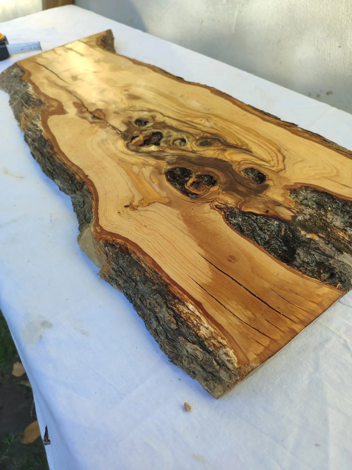 A rustic, light brown wooden slab with a natural bark edge and dark knot patterns.